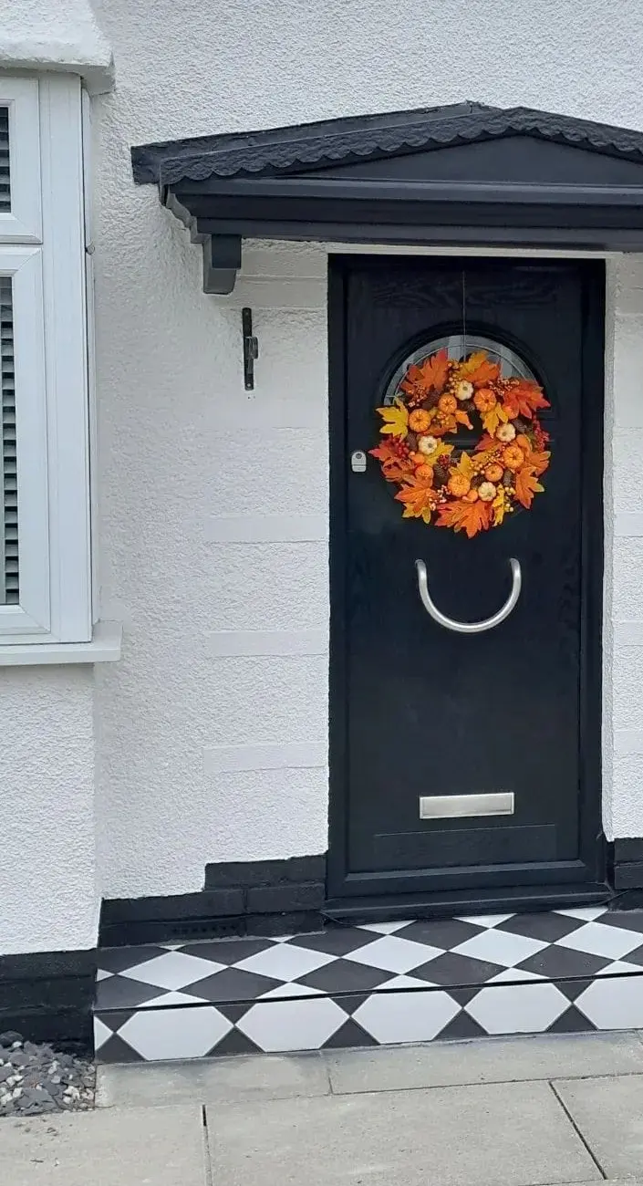 Black front door with a canopy, white rendered wall and a black and white tiled doorstep