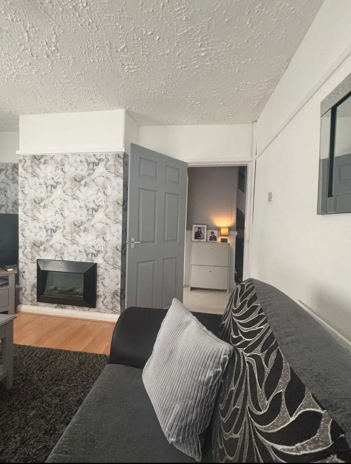 Living room with a patterned wallpaper feature wall around a fireplace, grey door and dark sofa